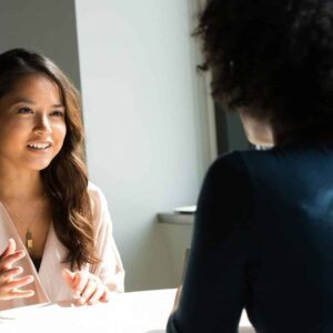Two women sitting at a table having a professional discussion in a bright office setting.